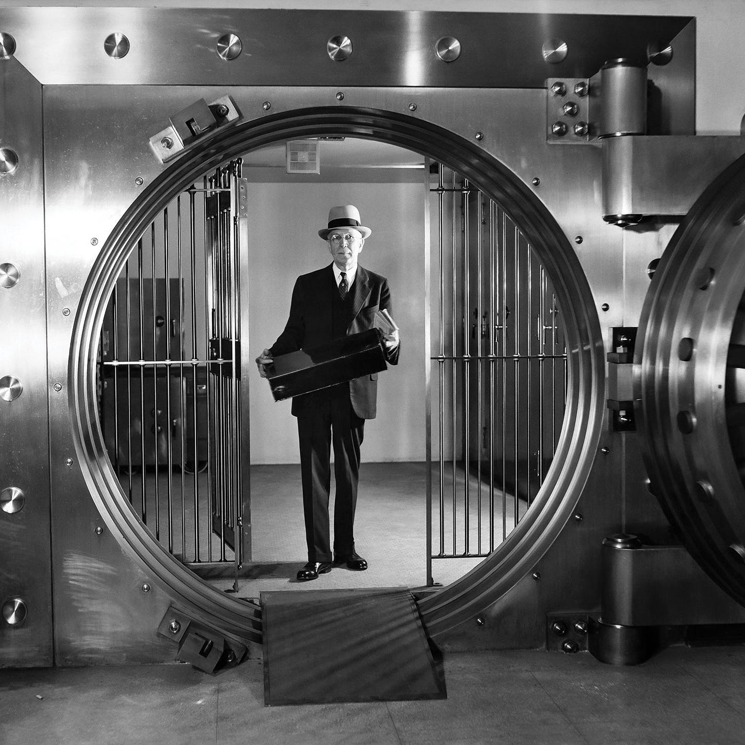 Vintage black and white photo of a man holding a box behind a bank vault door