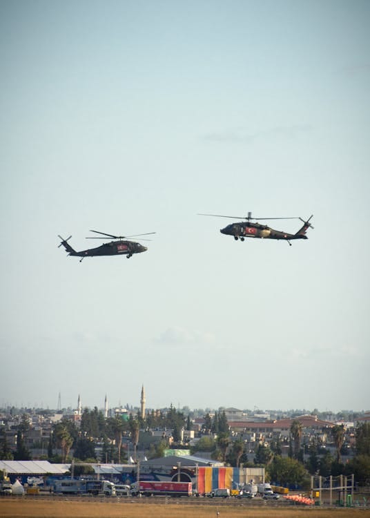 Free Two military helicopters hover above a city, offering a striking scene against the open sky. Stock Photo