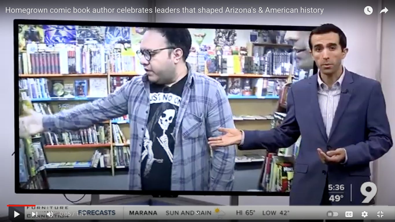 Screenshot of KGUN 9 reporter gesturing to a screen of Henry Barajas in a purple and grey plaid longsleeve over a black shirt with a grim reaper making the shush motion. Henry is in a comic book store surrounded by graphic novels.