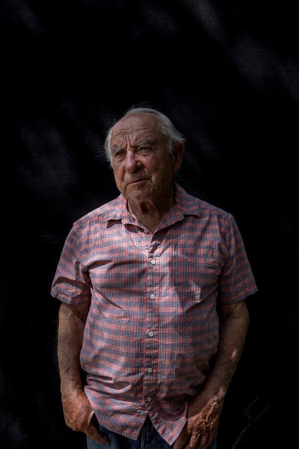 83-year-old Yvon Chouinard, the CEO of Patagonia, stands with his hands in his pockets wearing a red and blue checkered button-up shirt. 