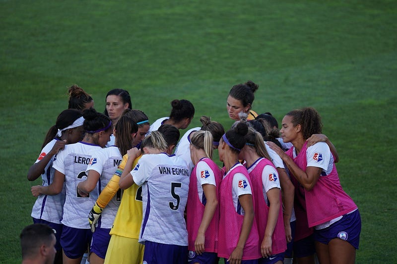 A female sports team coming together on the field for a team huddle.