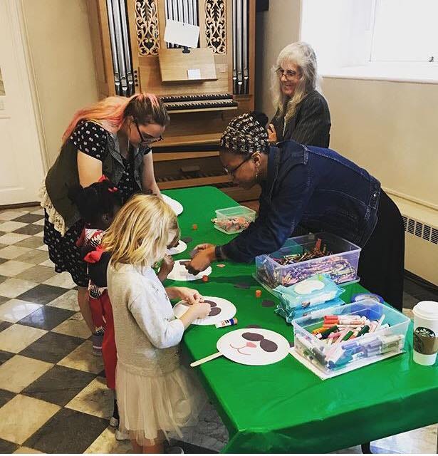 Several adults help children make panda crafts inside a church.