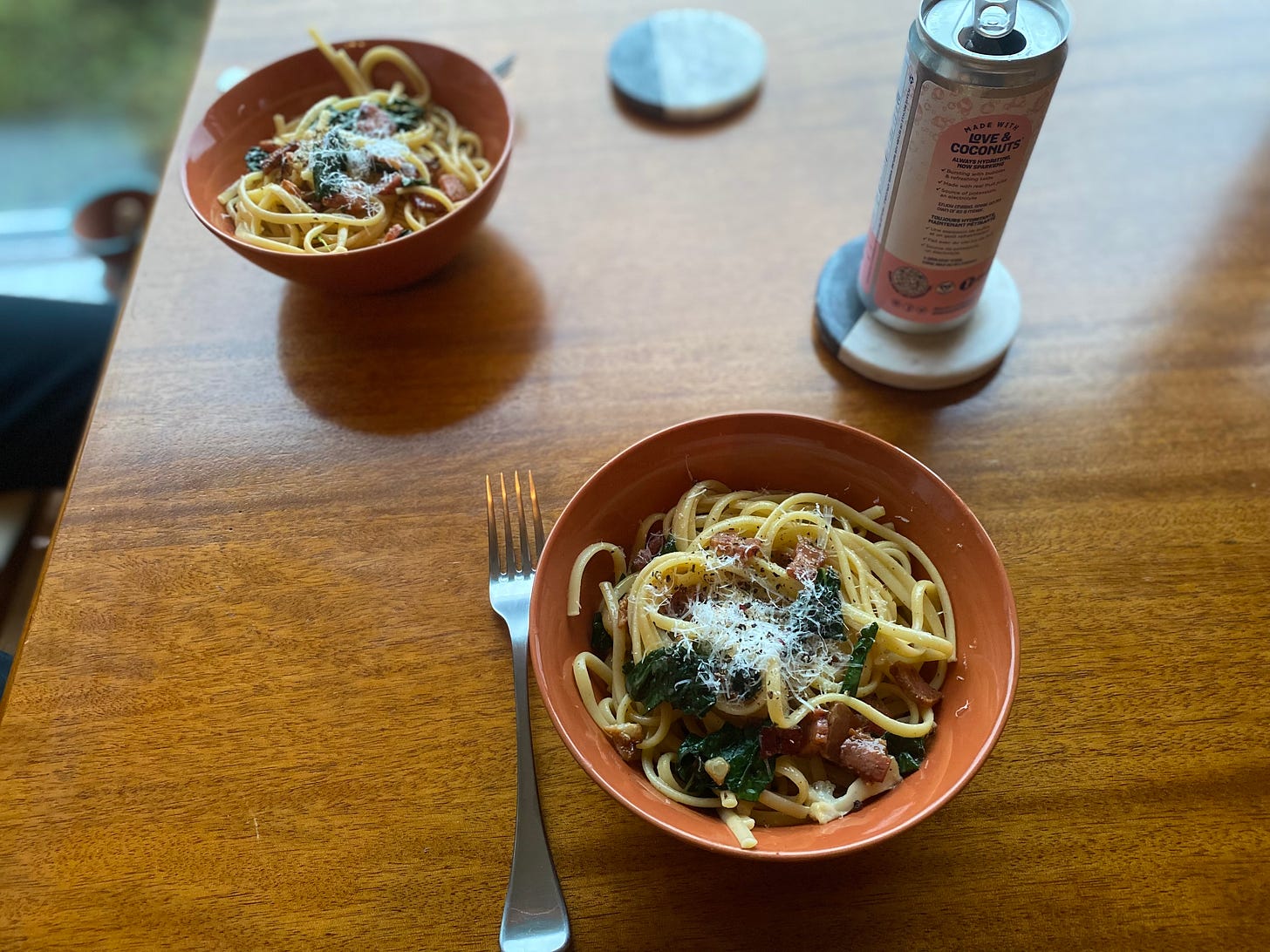 Two orange bowls of the pasta described above: chopped bacon, cauliflower pieces, dark green kale leaves in linguine with parmesan and black pepper on top.