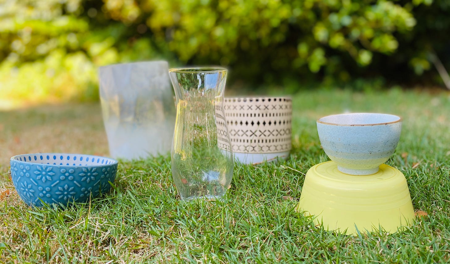 different bowls and vases sit on some grass