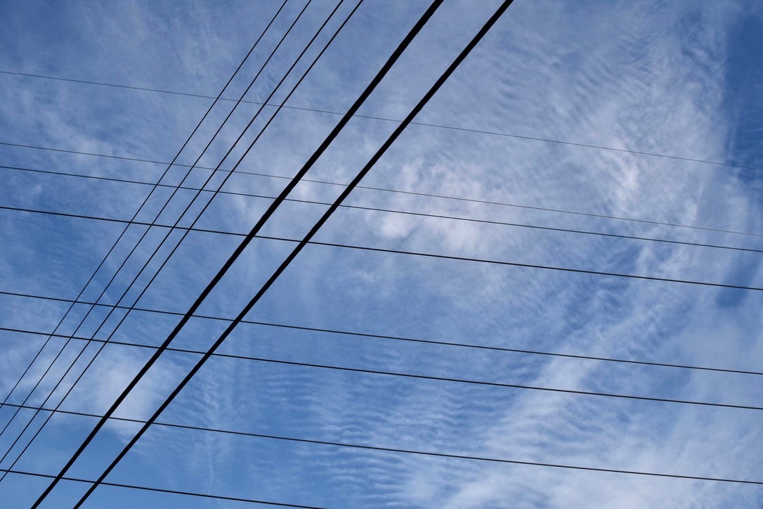 crisscrossed power lines beneath a thinly-clouded sky