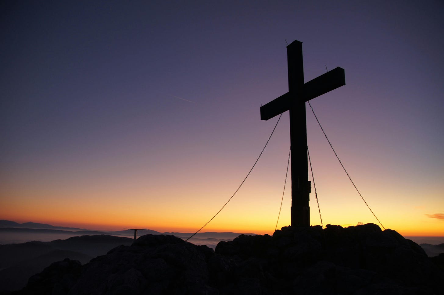 A large shadow of a cross haunts a beautiful orange and dark purple sunset. 