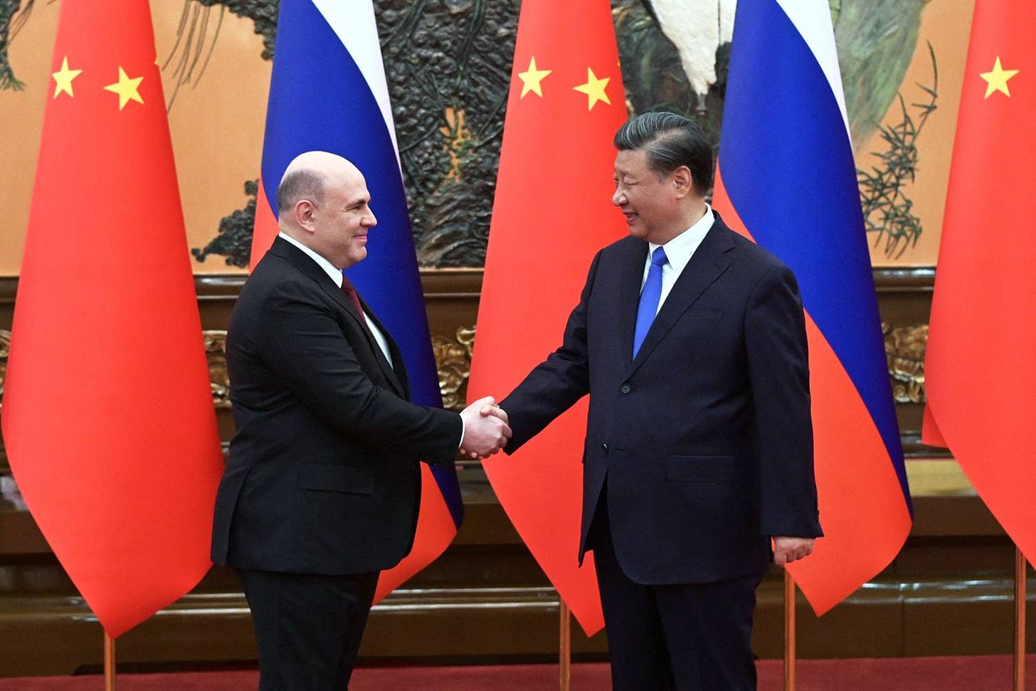 Mishustin and Xi shake hands in front of a row of alternating Chinese and Russian flags