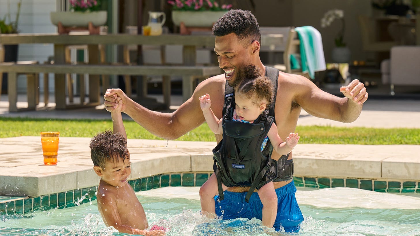 dad and two kids playing the pool and dad is wearing an aquaroo carrier