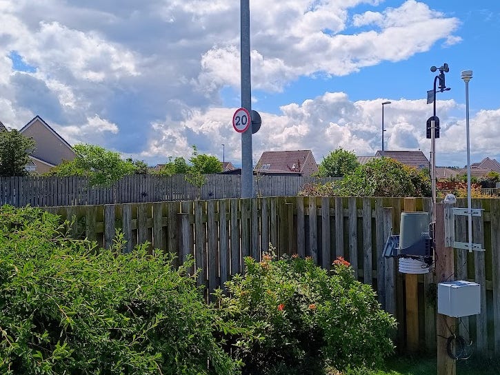 20mph speed limit sign on a lamp post viewed over a garden fence