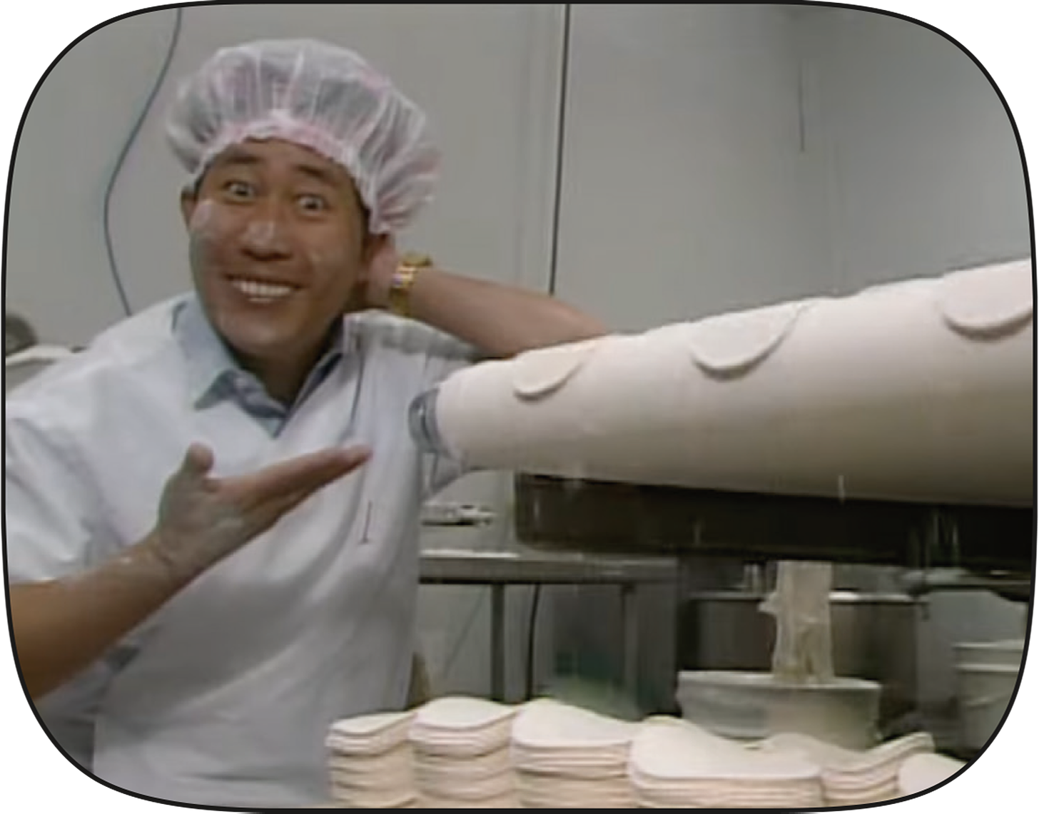 Martin Yan points at potsticker wrappers as they fall off of a conveyor belt.