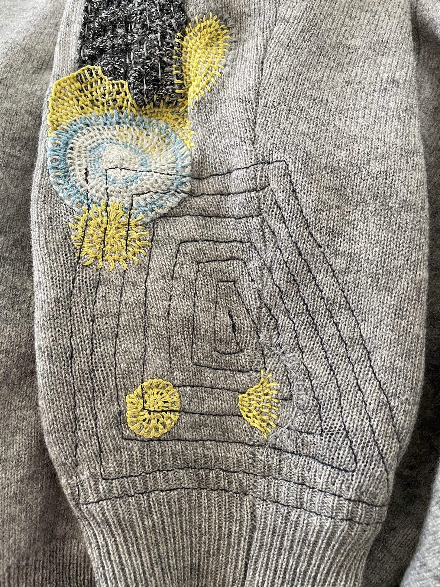 Sleeve of a gray cashmere sweater. It's visually mended with appliques, blanket hand stitches, and machine stitches.