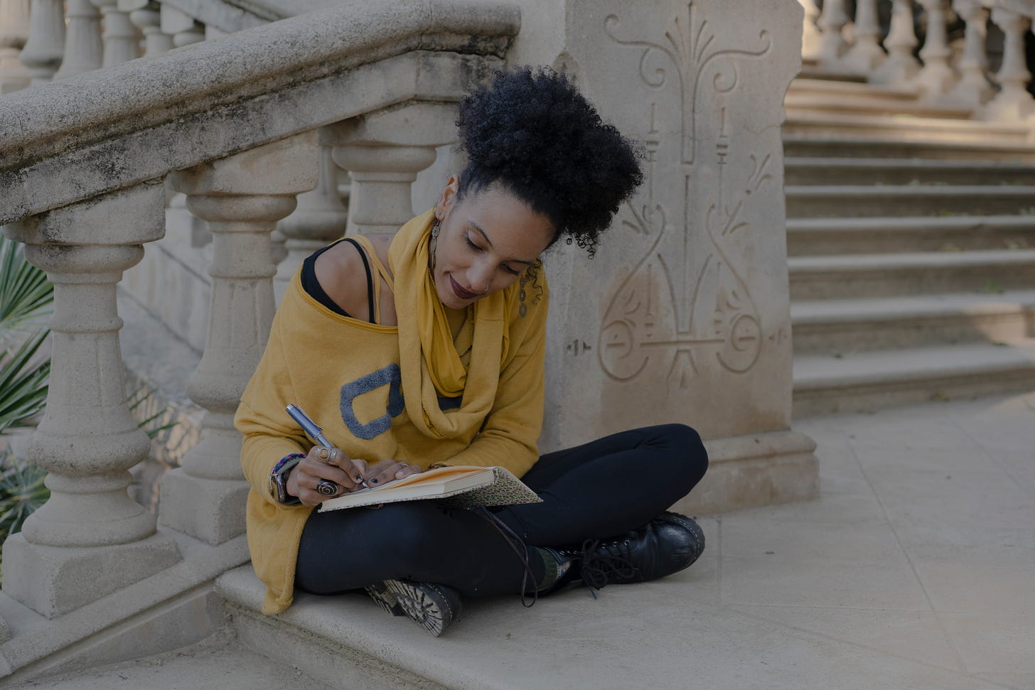 Woman sitting outdoors on stone steps writing on a journal.