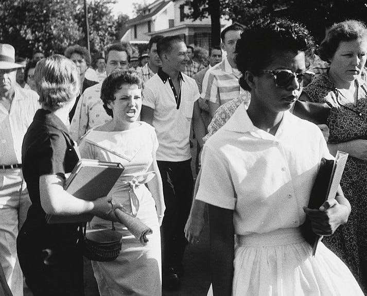 a young black female student walks into school with a crowd of white students behind her. One white female student is angry and yelling at her.