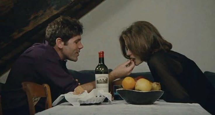 This may contain: a man and woman sitting at a table with food in front of them, looking at each other