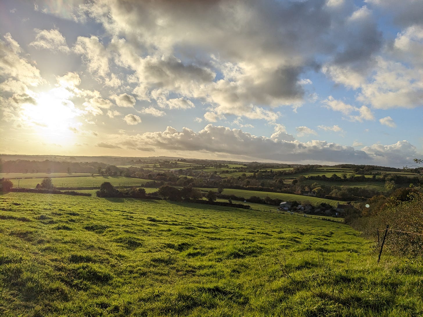 A view over green fields in Somerset with a sky scattered with clouds