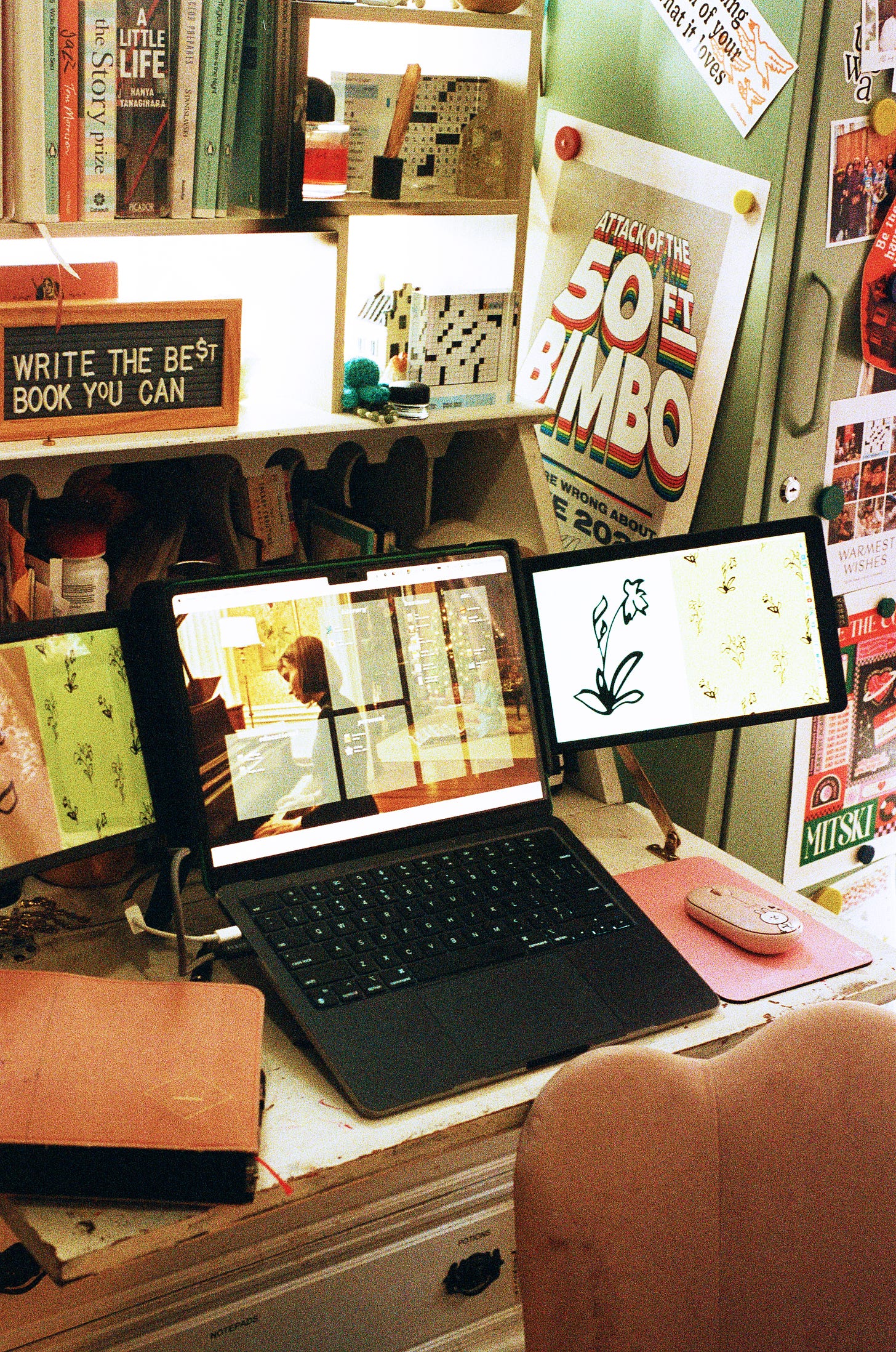 a desk with a laptop on it open to a Carol wallpaper, lots of books on top of the desk, and a sign on it that says "write the best book you can"