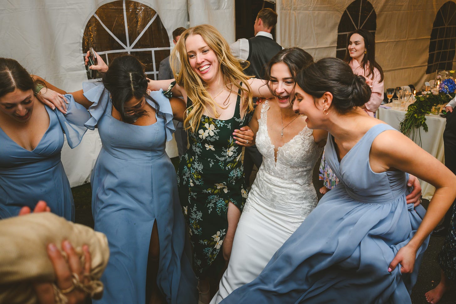 A bride, some bridesmaids, and some guests dancing arm-in-arm