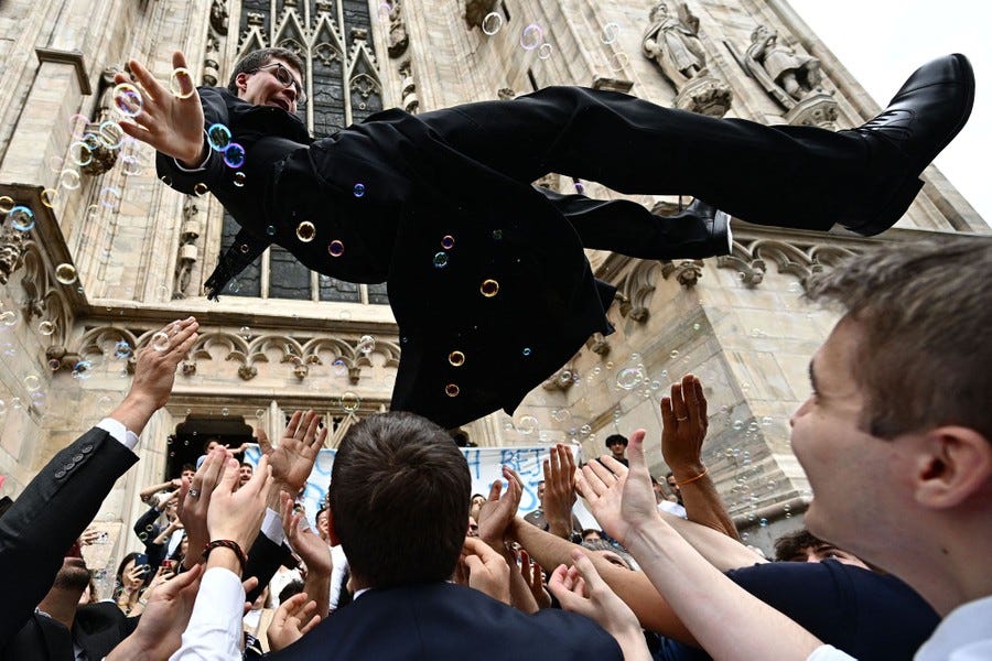 A group of people toss one person in the air in front of a cathedral.