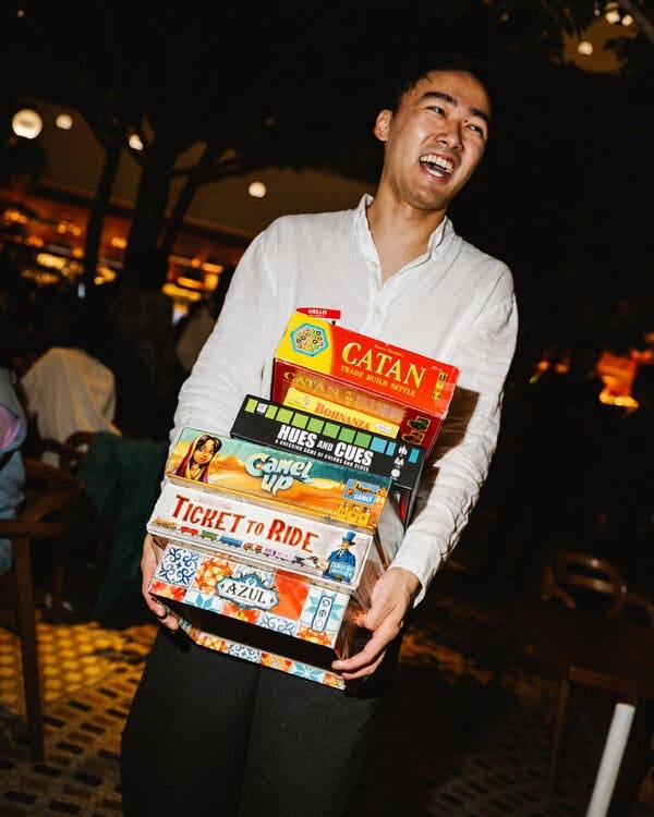 Richard Ye carries a large stack of board games, including “Ticket to Ride” and “Camel Up.”