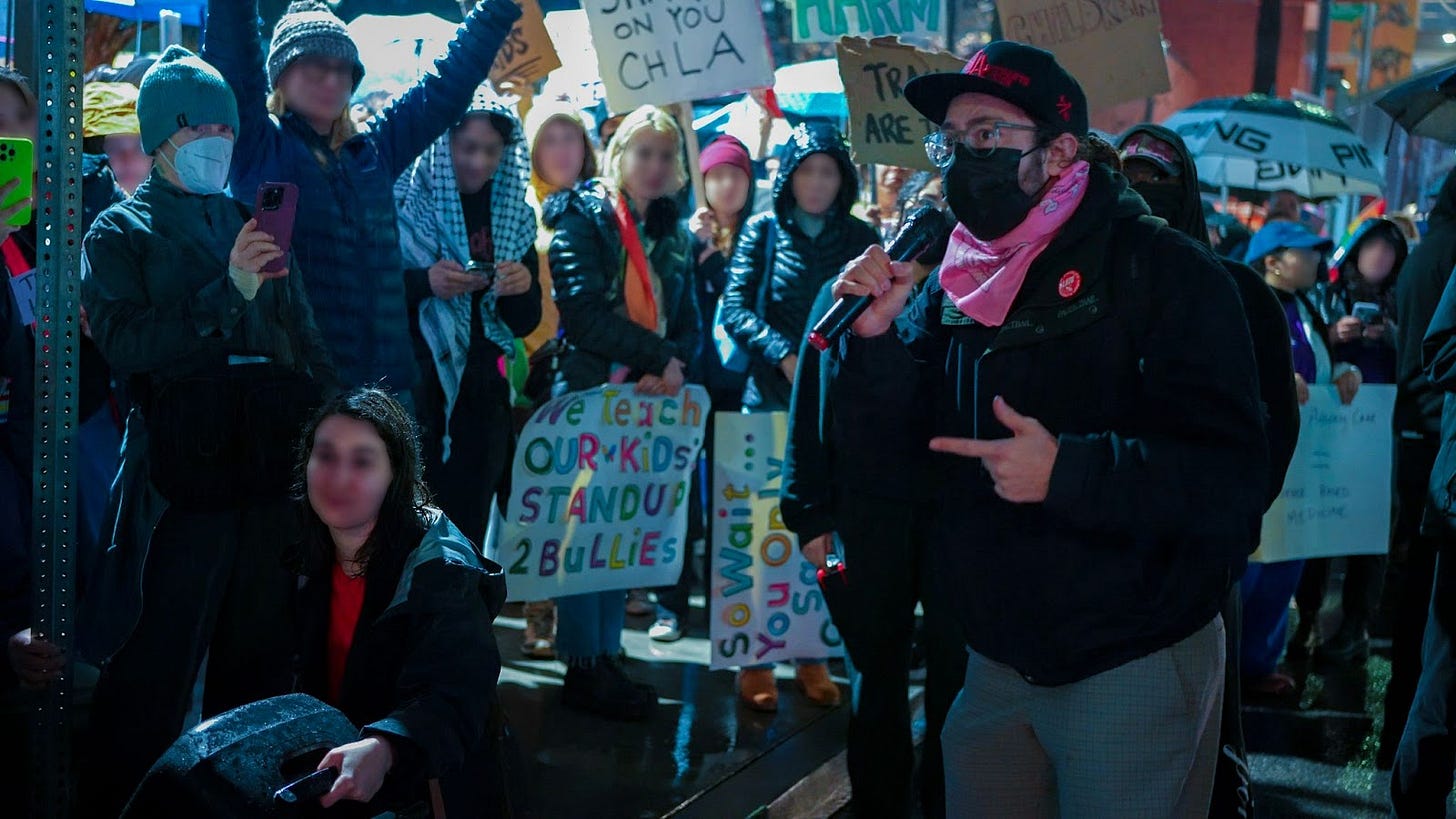 Joe Holldendoner holds a microphone as he speaks to a blurred crowd of protestors at a CHLA protest Joe Holldendoner holds a microphone as he speaks to a blurred crowd of protestors at a CHLA protest