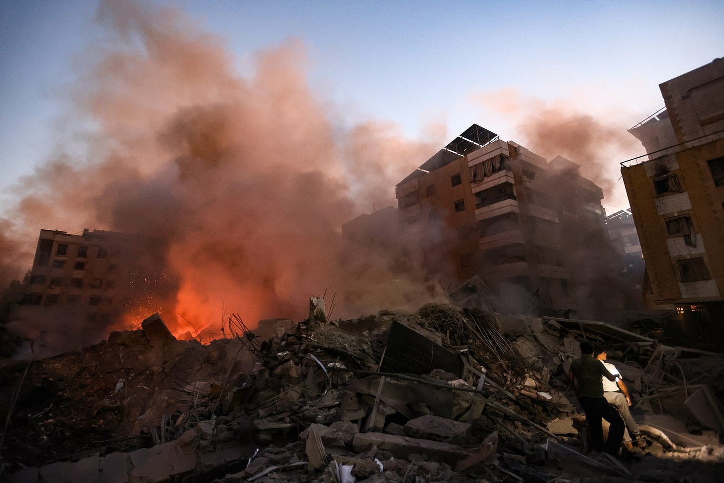 A photograph of aftermath of Israeli air strike in Beirut Lebanon. Smoke is seen rising from rubble and a fire in the...