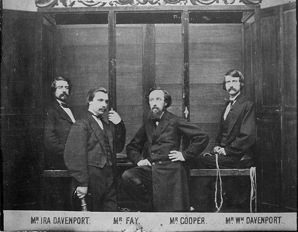 Four gentlemen, two seated, in front of a large wodden cabinet