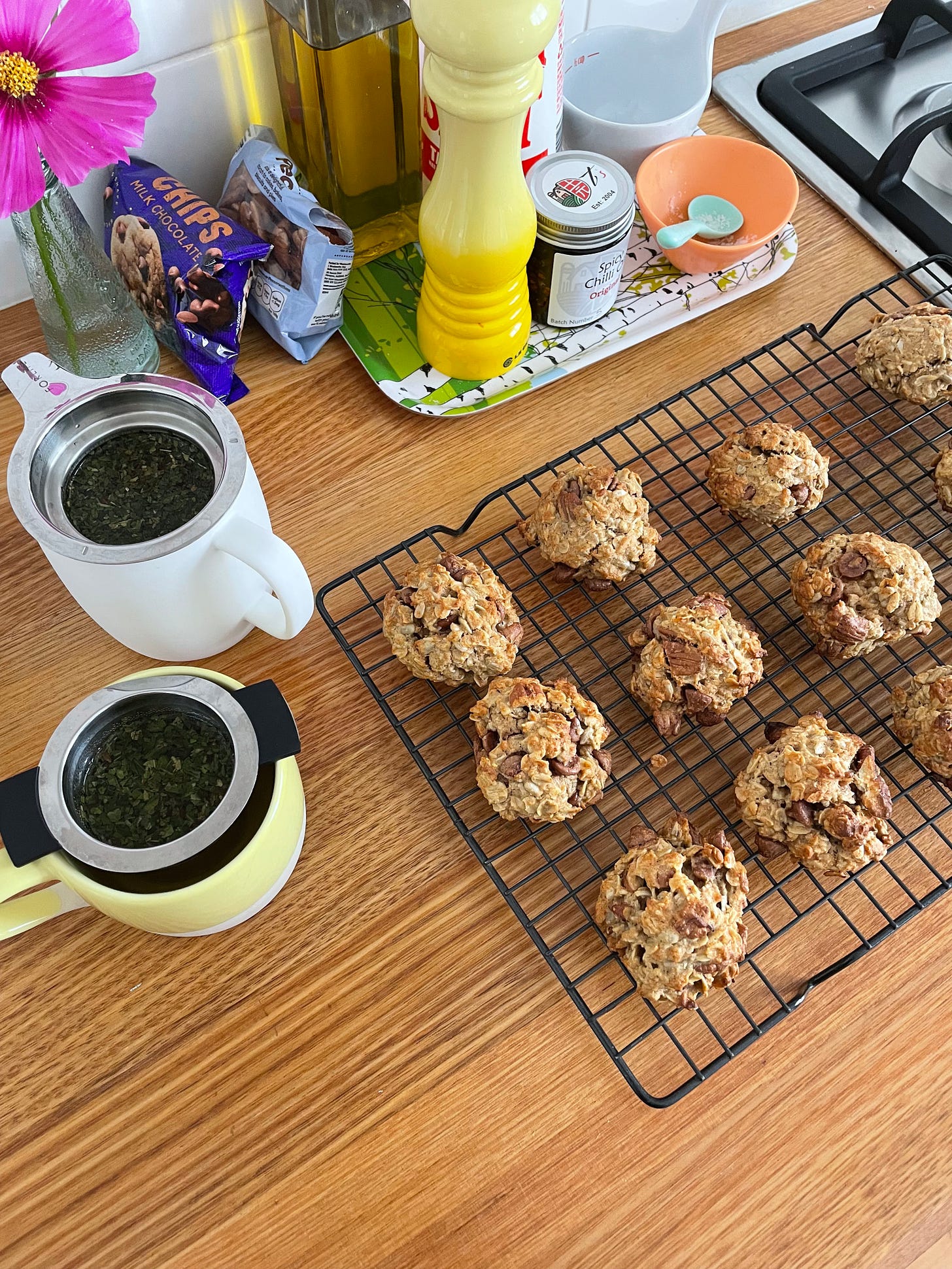 Batch of granola cookies cooling on a wire rack with two peppermint teas nearby. A kitchen scene.