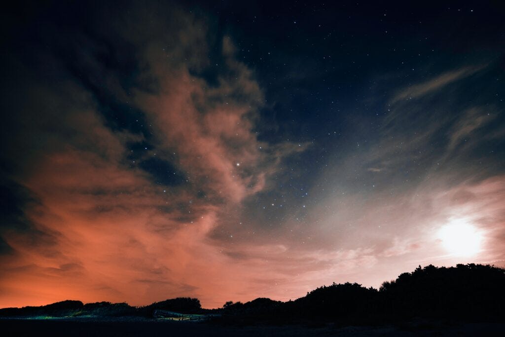 Pink lighted clouds at the horizon under a blue-black sky twinkling with stars