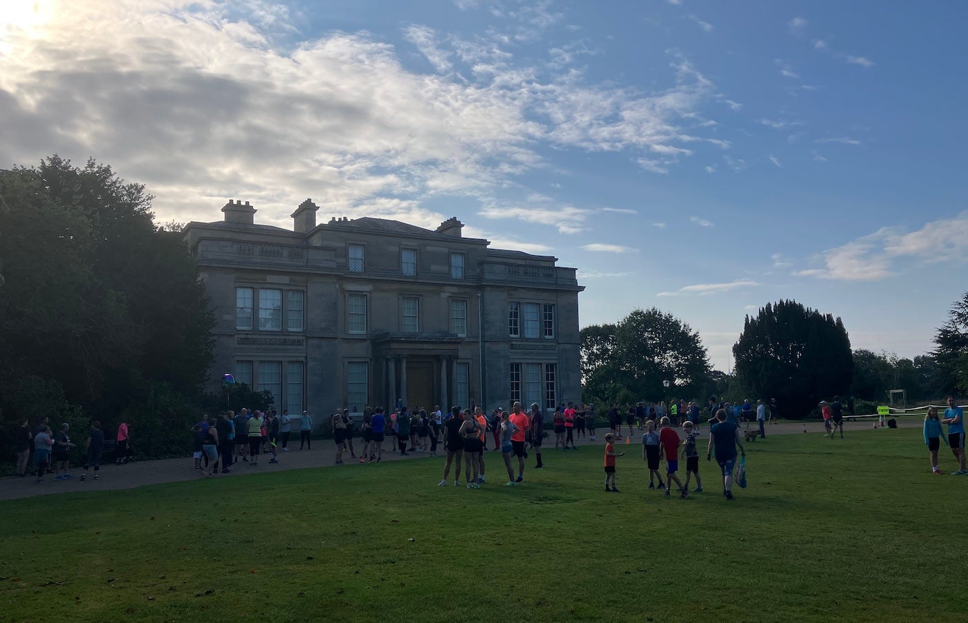 Normanby Hall under cloudy blue sky looking over a large lawn with parkrunners gathering