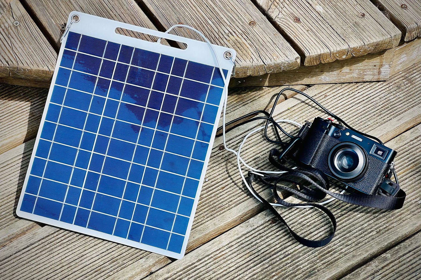 A photograph of a small semi-flexible solar panel plugged into a Fuji film X100iv