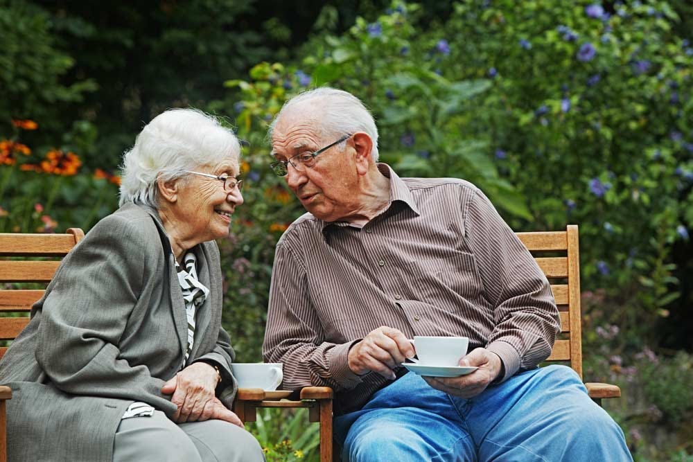 Elder couple savoring their cups of coffee while enjoying an outdoor garden space.