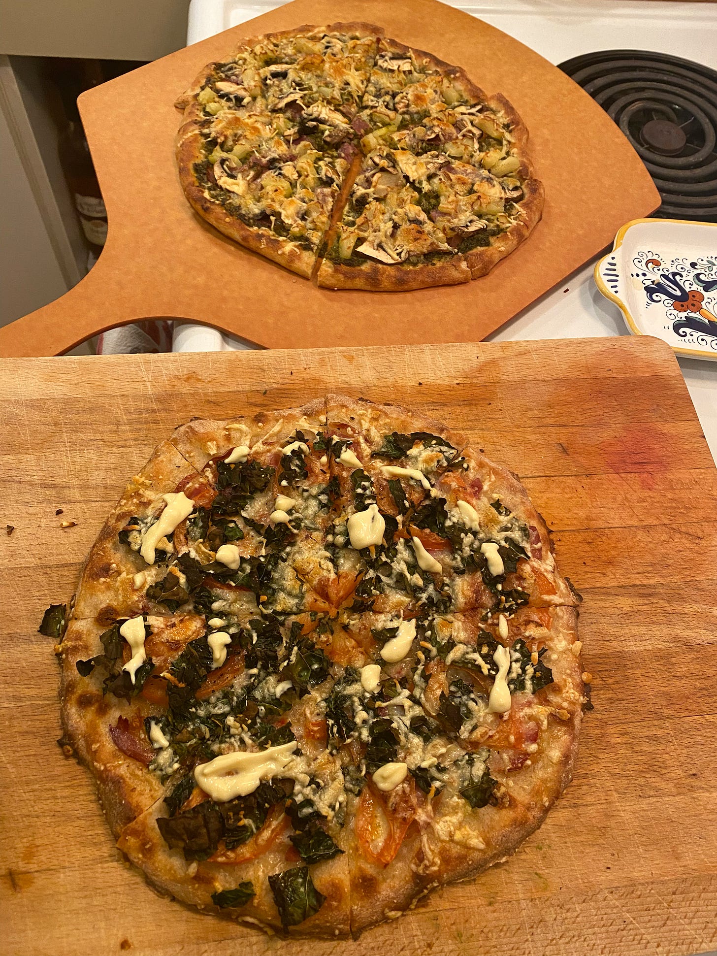 Two pizzas, one on a pizza peel, and one on a cutting board. They are browned on top at at the edge of the crust.