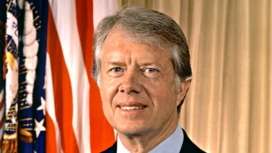 Official photo of Carter during his presidency, zoomed in on his face, flag on the background.