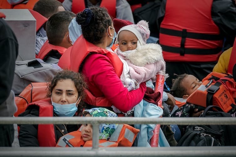 Close up of two women and their children on a Border Force vessel, wearing red life jackets.