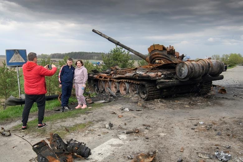 People pose for a picture in front of the debris of Russian military machinery in the village of Rusaniv, Kyiv region, Ukraine, April 25. REUTERS/Vladyslav Musiienko