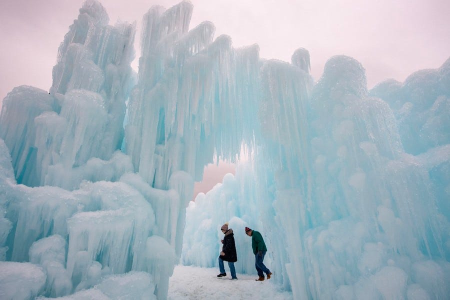 Two people walk beside tall sculptures made of icicles and ice chunks.