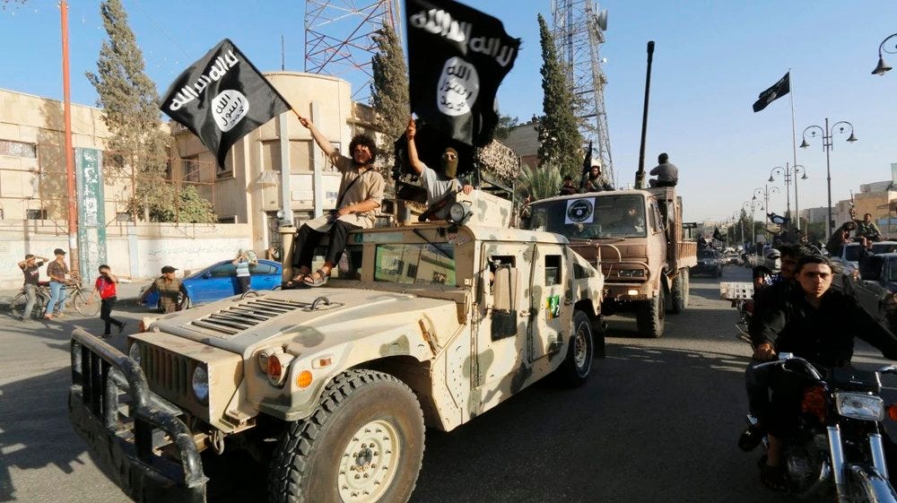 ISIS militants waving flags while driving through a city in armoured vehicles.