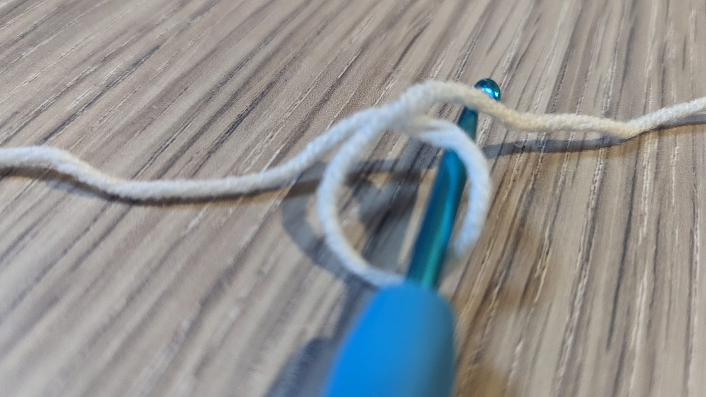 A crochet hook entered into the loop, with the hook over the short end of the yarn