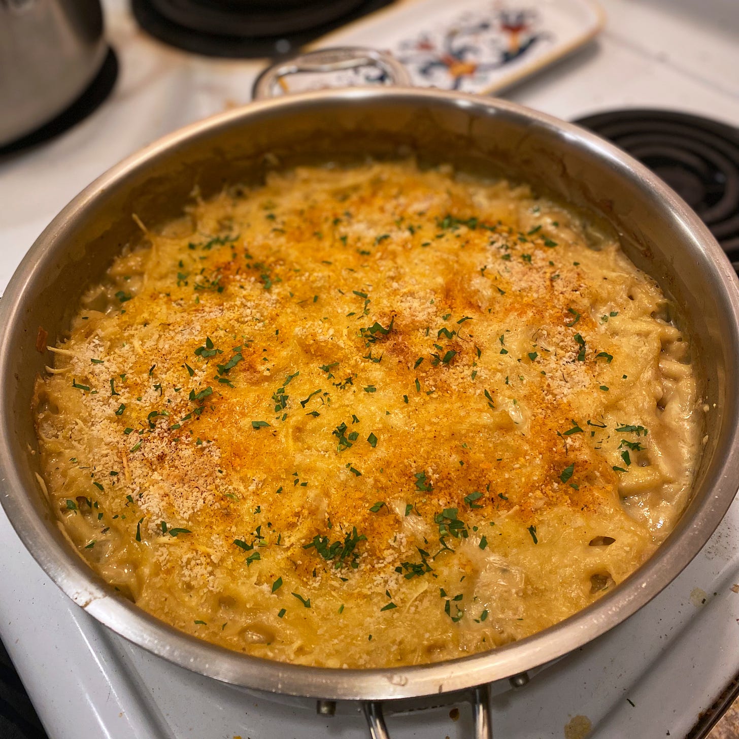 A large stainless steel pan of squash mac & cheese, the top crusted with panko crumbs and browned cheese, sprinkled with parsley.