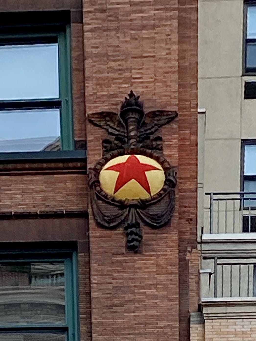 Decorative mason work of a red star in a cream oval with an engraved, winged torch above it.