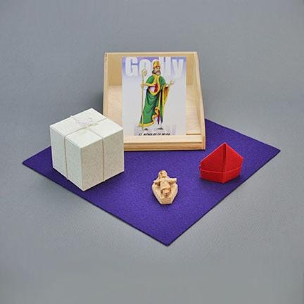 The Godly Play St. Nicholas story, featuring an image of St. Nicholas, a white gift box, a red bishop's hat, and the wooden baby Jesus figure from a nativity set on a purple underlay.