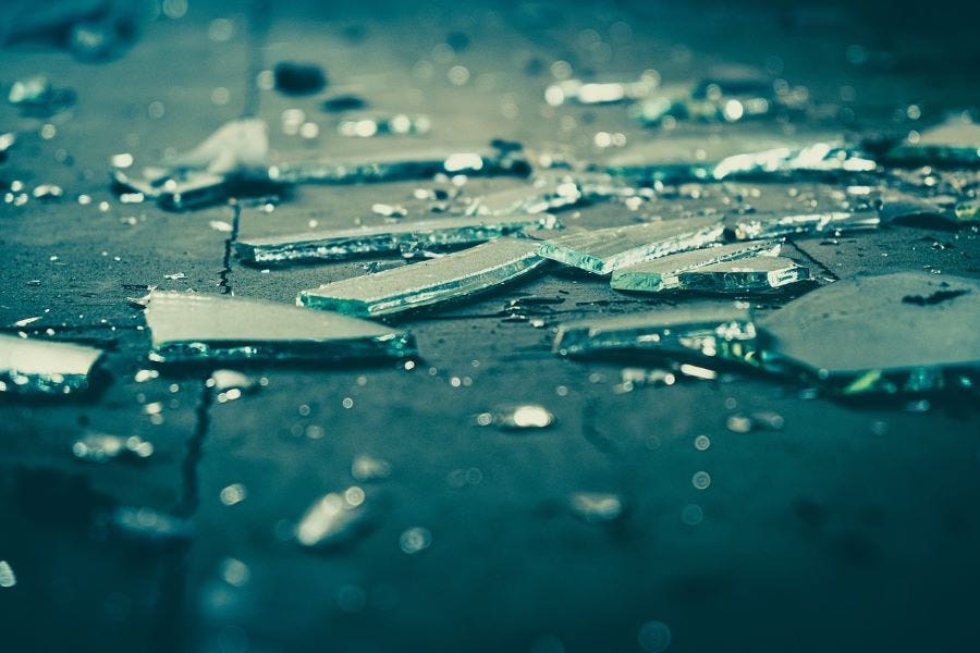 Shards of glass of various sizes lying on a sidewalk.