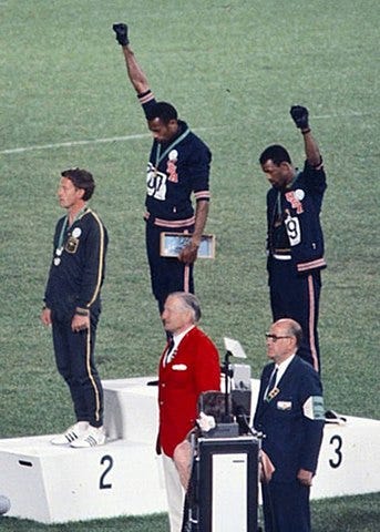 It’s that famous photo from when American track athletes Tommie Smith ’n’ John Carlos were on the Olympic podium, raisin’ their hands in Black Power salutes. The other guy in the photo, in case ya were curious, is an’ Australian fella named Peter Norman.