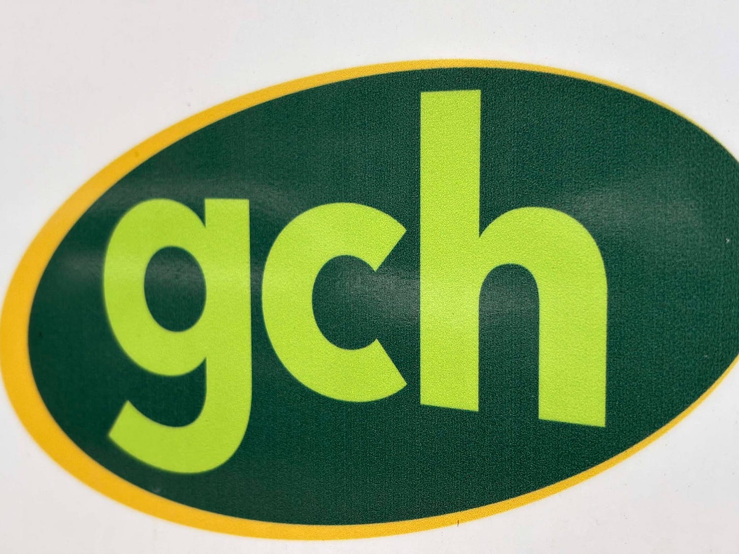 The picture shows the logo of Gloucester City Homes. It is an oval shape with a yellow outline, dark green fill and the letters GCH are coloured light green