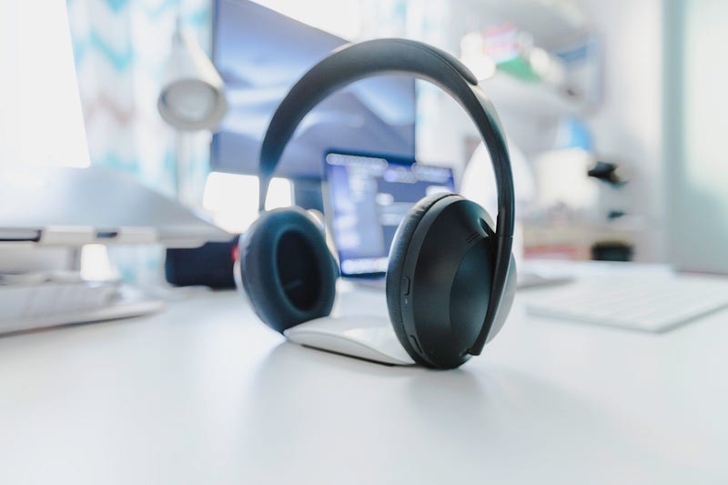 a pair of over-ear headphones, balanced upright on an Apple mouse a pair of over-ear headphones, balanced upright on an Apple mouse