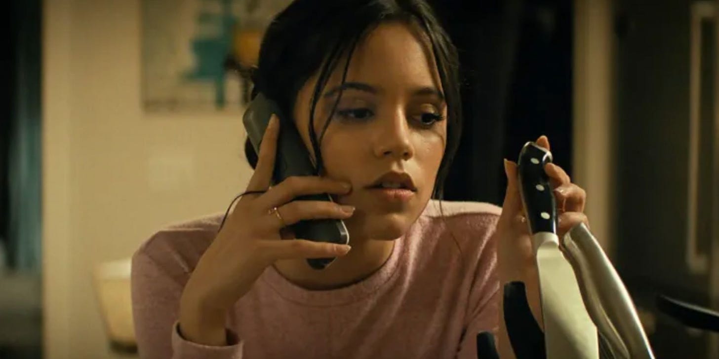 Jenna Ortega on the phone, looking at a kitchen knife, from Scream.