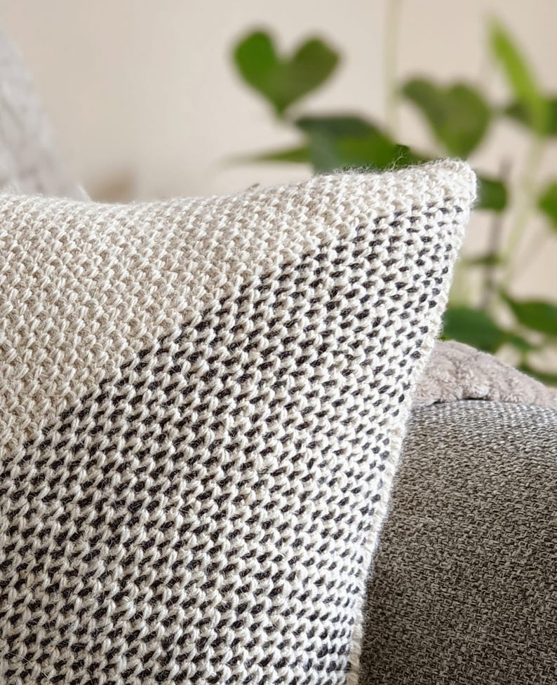 Close up of the corner of a white and black diagonal-stripe pillow on a grey couch