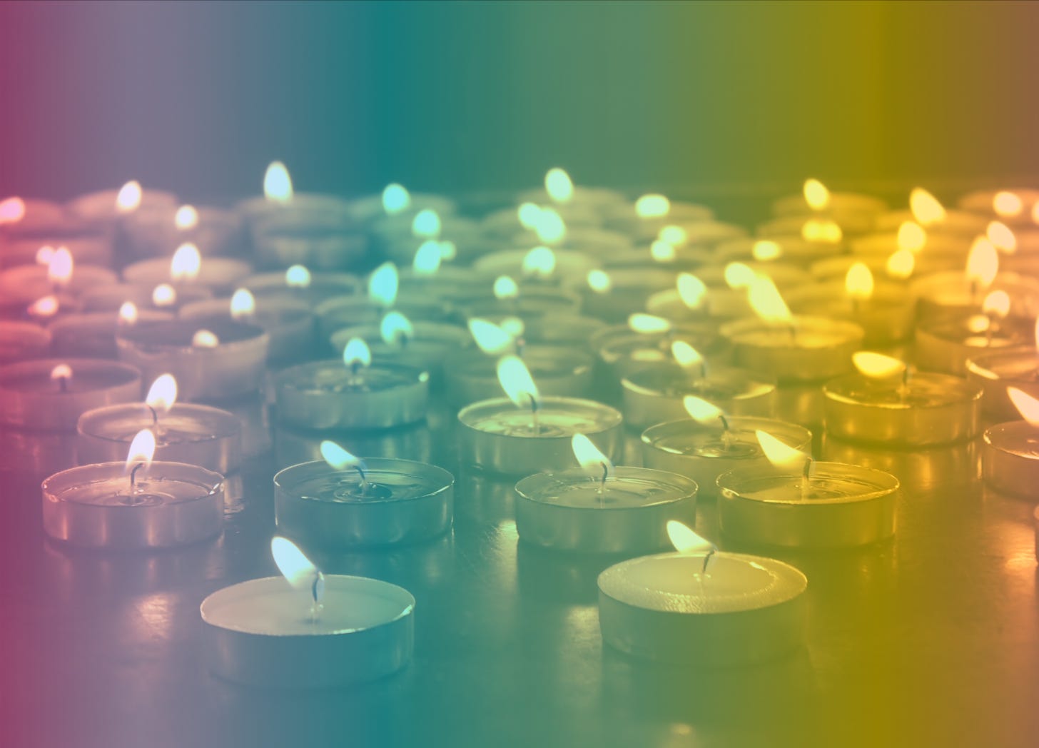 A rainbow-filtered photograph of dozens of lit tea candles