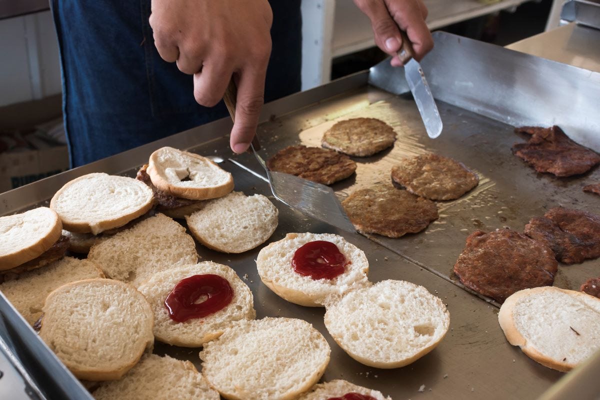 Closeup of flipping burger patties and warming buns on an old griddle at a burger joint