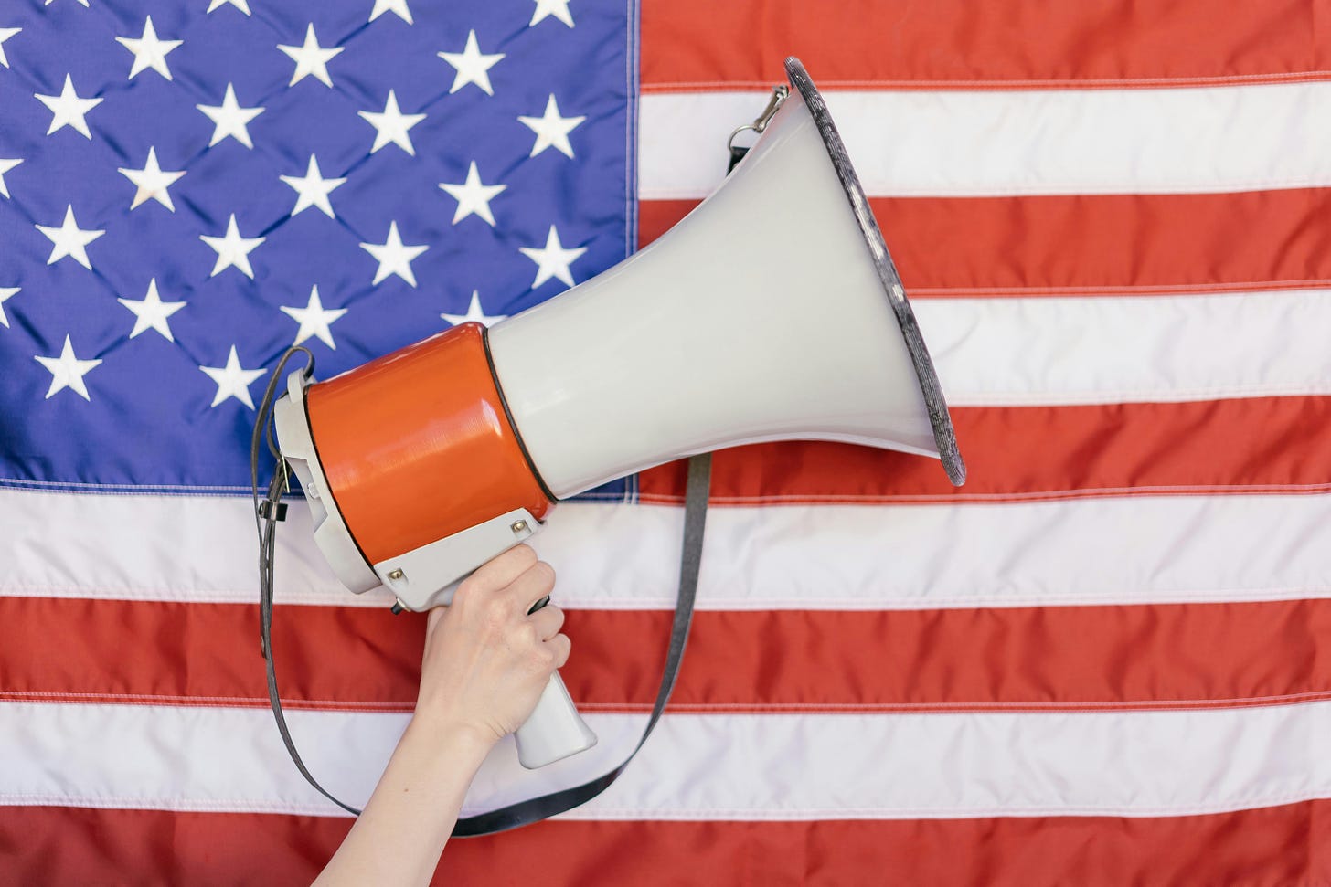 A pale hand hods up a megaphone in front of an American flag.